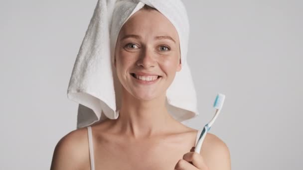 Mooi glimlachend meisje met handdoek op hoofd met tandenborstel zwaaiend met ja gebaar op camera over grijze achtergrond. Advies het uit te drukken - Video
