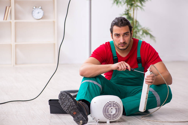 Jovem empreiteiro masculino reparando aquecedor de ventilador dentro de casa
 - Foto, Imagem
