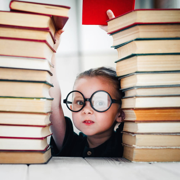 Cute little girl taking a book from top of books tower. Reading and kids education concept. - Photo, Image