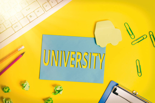Text sign showing University. Conceptual photo an educational institution designed to teach and investigate Flat lay above empty paper with copy space and colored paper clips. - Photo, Image