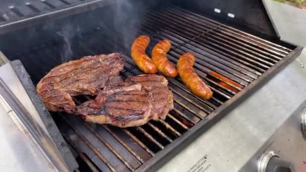 Lifestyle summer outdoor man cooking stakes and sausages on a propane gas grill holing metal tongues - Footage, Video