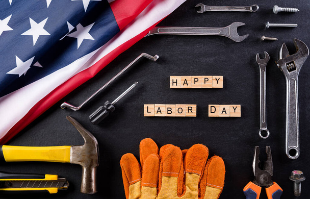 Happy Labor Day concept. Amerikaanse vlag met verschillende bouwgereedschap op zwarte tafel achtergrond, met kopieerruimte voor tekst. - Foto, afbeelding