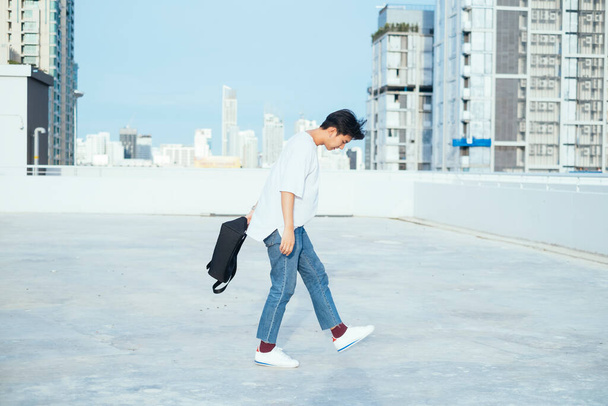 Teini-ikäinen kaveri farkuissa ja valkoisessa t-paidassa kävelee kaupungin korkean rakennuksen katolla yrittäen vähentää hänen vihaansa.. - Valokuva, kuva