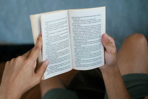 Περικοπή εικόνας του ανοιγμένου βιβλίου στα χέρια ενός ανθρώπου, ενώ το διάβαζε. - Φωτογραφία, εικόνα