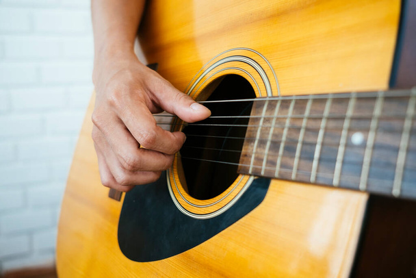 Gehakt beeld van gitaar met muzikant hand op het klankgat terwijl hij het lied speelt. - Foto, afbeelding