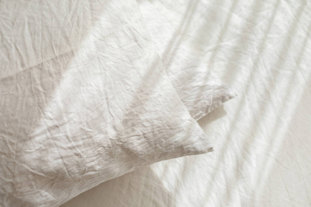White linen textile bedclothes. Pile of pillows. Cozy bedroom interior and beautiful morning light. Pastel color. Trendy organic natural linen. - Photo, Image