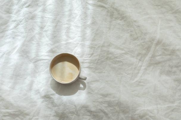 Cup of fresh coffee on texture of linen cotton rough textile bedclothes. Morning mood. Cappuccino in bed. Empty place, copy space. - Valokuva, kuva