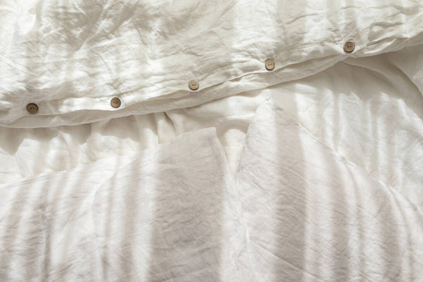 Trendy organic natural linen bedclothes with wooden buttons closeup. Bedding, morning light, bedroom style and design. Rough textile background with wrinkle. - Photo, Image