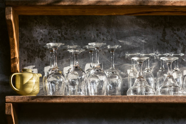 Set of different champagne, wine, martini empty clean glasses on bar restaurant wooden shelf. Gray concrete wall, loft interior design. Shining sun light. - Foto, afbeelding