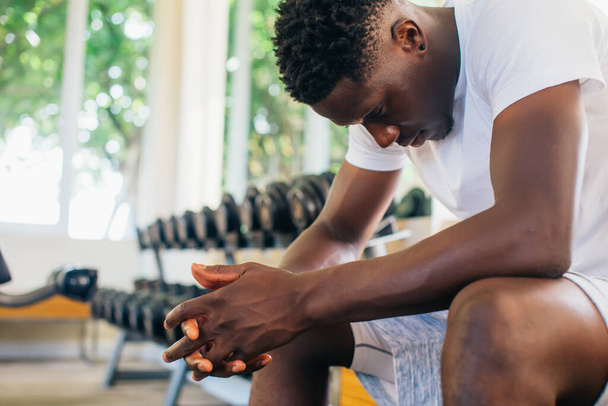 Desperate African American man sitting on bench during break in fitness training in modern gym - Photo, Image