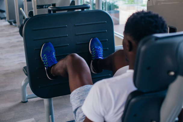 Back view of African American man doing exercise on leg press during fitness training in modern gym - Φωτογραφία, εικόνα