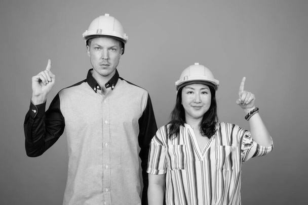 Young businessman and mature Japanese businesswoman together against gray background in black and white - Photo, image
