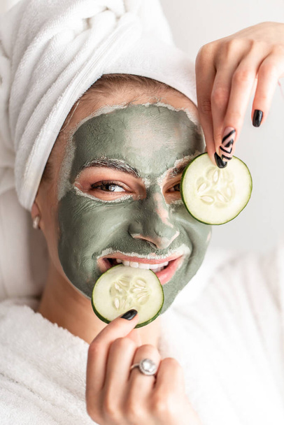 Close-up portrait young woman with a clay mask. covering her eyes with cucumber. detox cosmetics concept. - Foto, imagen