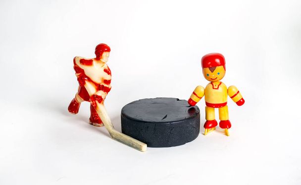 Hockey. Zwei rote Toy-Hockey-Spieler stehen neben dem Puck. Kinderhockey, ein Symbol für Sporthockey. Isoliert auf weißem Hintergrund. - Foto, Bild