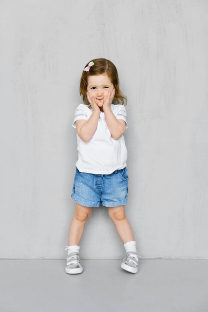 Two years old girl in white t-short and jeans shorts posing in studio - Photo, Image