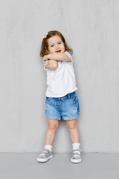 Two years old girl in white t-short and jeans shorts posing in studio - Foto, immagini