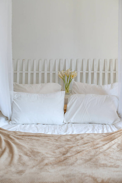 Útulná světlá ložnice v bílých a béžových barvách. Interiér je ve stylu minimalismu. Postel s bílým povlečením na ranním slunci. Ekostyl a přírodní materiály - Fotografie, Obrázek