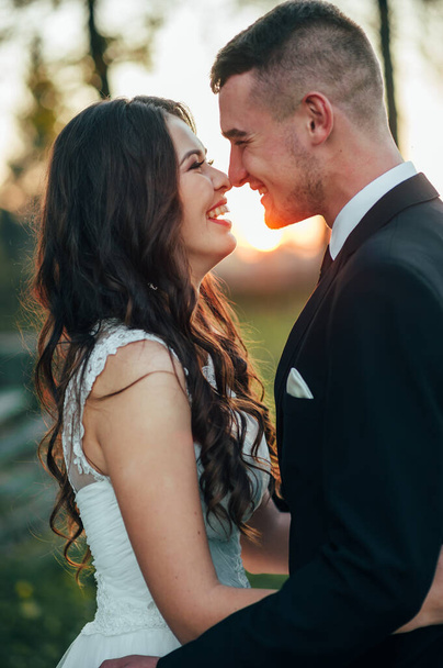 Sunshine portrait of happy bride and groom outdoor in nature location at sunset. Warm summertime. Happy couple with a beautiful bouquet of flowers. Wedding photo. Couple in love. Autumn wedding - Zdjęcie, obraz