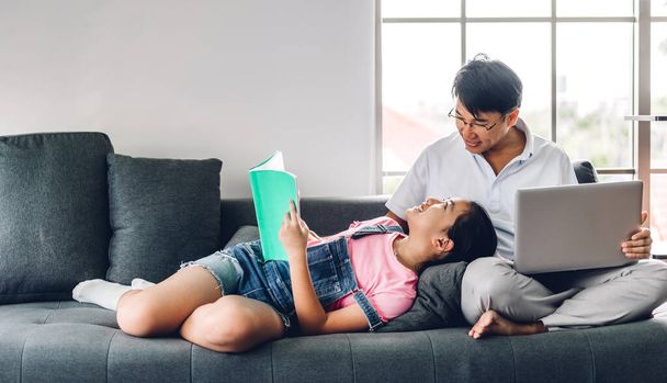 ノートパソコンを使ってリラックスしているアジア系男性の笑顔と、娘が本を読んで家で知識を勉強している様子とのビデオ会議。 - 写真・画像