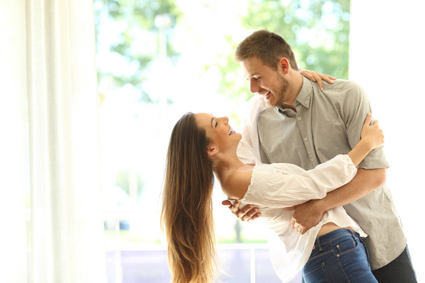 Happy couple flirting and dancing together standing in the living room at home - 写真・画像