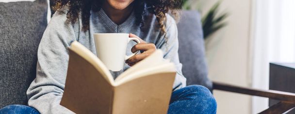 Giovane hipster afro-americana donna nera rilassante leggendo il libro di carta studio di lavoro e guardando rivista pagina mentre seduto sul divano a casa - Foto, immagini