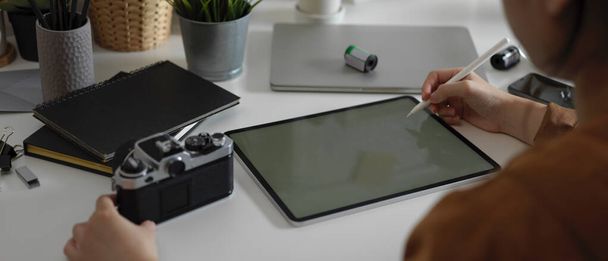 Fotografía recortada de una fotógrafa que trabaja en una tableta simulada con lápiz óptico y cámara en la mesa con suministros en el estudio
 - Foto, Imagen