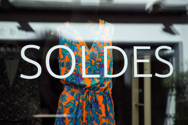Closeup of discount sign "SOLDES " in french,  the traduction of  (sales ) on window in french fashion store showroom on summer clothes background - Fotoğraf, Görsel