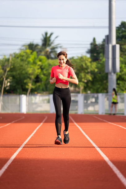 Young fitness woman runner jogging excercise in the morning on stadium track in the city. Female athlete excercise in the city stadium to keep body fitness during COVID-19 pandemic. Health and recreation stock photo. - Foto, Imagen