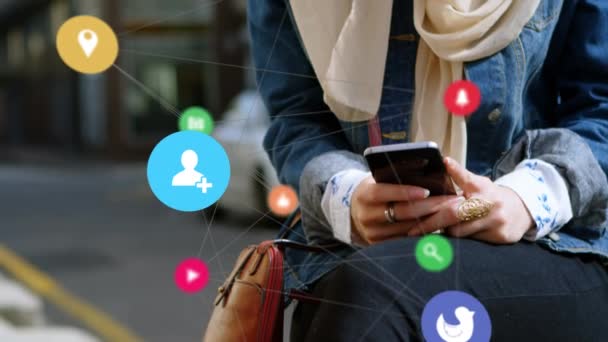 Animation of icons floating with web of connections over mixed race woman wearing hijab and using smartphone. Social networking global connections concept digital composite. - Πλάνα, βίντεο