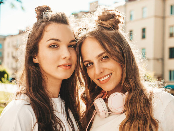 Closeup portrait of two young beautiful smiling hipster girls in trendy summer white t-shirt clothes.Sexy carefree women posing on street background. Positive models looking at camera. Beauty concept - Foto, Imagen