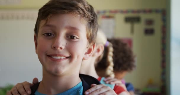 Portrait of caucasian boy standing with his classmates in a row with hands on each others shoulders in classroom, looking at camera and smiling, in slow motion. education at an elementary school. - Video, Çekim