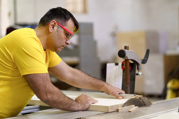Male carpenter using saw for cutting wood at workshop - Photo, image