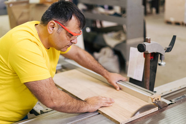 Плотник-мужчина с помощью пилы для резки дерева в мастерской - Фото, изображение