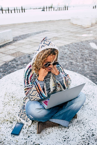 Концепция умной работы и цифрового образа жизни людей с жизнерадостной счастливой и свободной женщиной, работающей на улице с ноутбуком на ногах  - Фото, изображение