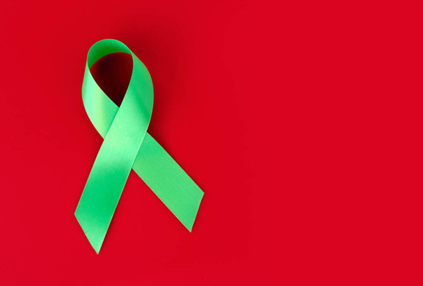 Green symbolic ribbon - the problem of organ donation, mental health. On a red background - Zdjęcie, obraz