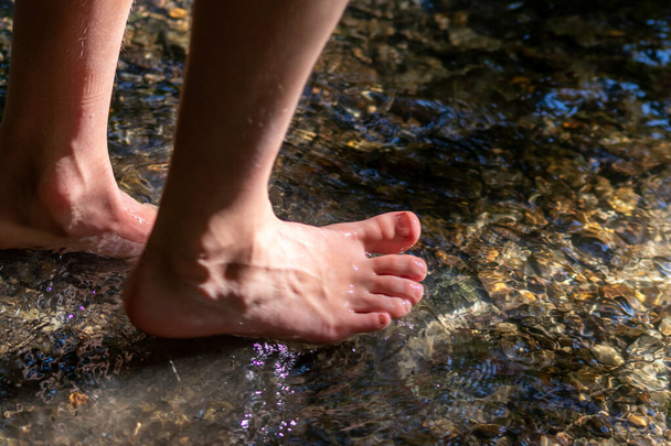 Küçük bir derede çıplak ayakla temiz suyla oynayan genç bir çocuk ayaklarını ve su kaynağını kullanarak ayak parmaklarını ve bacaklarını serinletiyor ve zen meditasyon atmosferindeki saf yaşam iksiriyle ferahlatıyor. - Fotoğraf, Görsel
