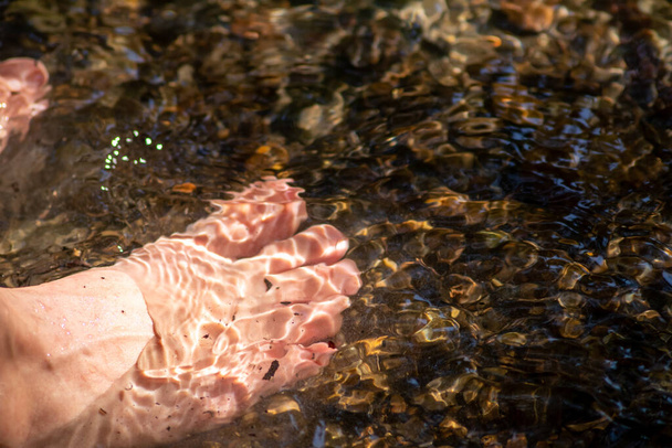 Niño jugando descalzo con agua clara en un pequeño arroyo usando sus pies y el manantial de agua enfriando sus dedos de los pies y piernas y refrescante con el elixir puro de la vida en la atmósfera de meditación zen - Foto, Imagen