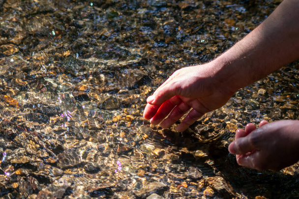 ヨーロッパの男性の手は、絹のような波紋と浮遊波と水の中に石を探して日当たりの良い反射と平らな小さな小川の透明な水の中に瞑想的な禅の雰囲気の中でさわやかな - 写真・画像