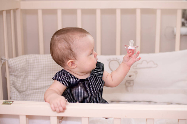 Menina bebê feliz brincando com uma chupeta em sua cama, em casa
 - Foto, Imagem