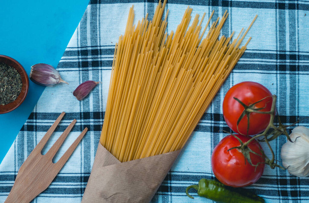 Tow tomatoes, garlic cloves pasta over cloth and wood fork with green pepper, vegetarian - Photo, Image