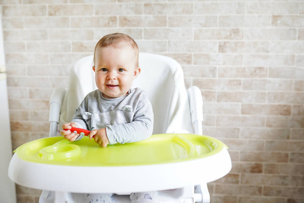 Μωρό με κουτάλι στην καρέκλα Στην τραπεζαρία, χαμογελαστό και χαρούμενο παιδί. φόντο με χώρο αντιγραφής - Φωτογραφία, εικόνα