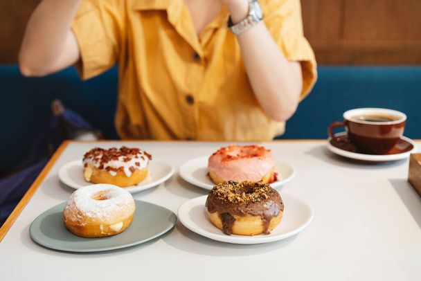Frau in gelbem Hemd, die Fotos von Erdbeerrosa, Schokolade, Zuckerglasur und Speck macht, Käse-Donut mit Glücksgefühlen in einem modernen Café. Genuss weiblichen Lebensstils. - Foto, Bild