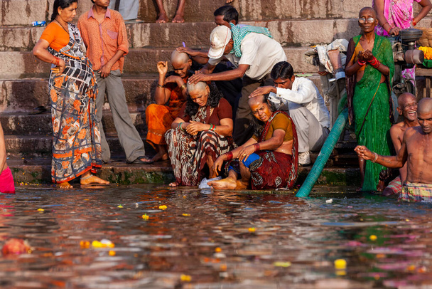 Männer, die Frauen die Köpfe rasieren und neben dem heiligen Wasser des Ganges sitzen. Varanasi, Indien - Foto, Bild