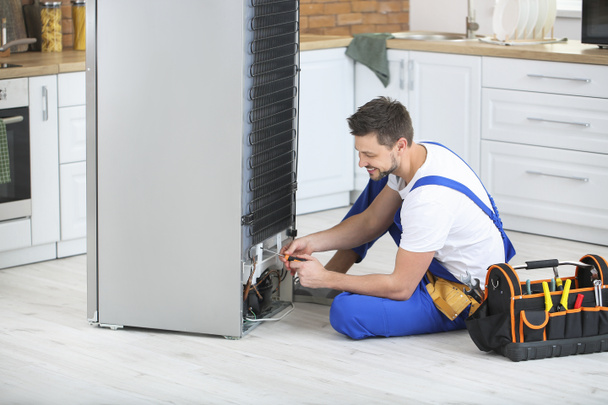 Worker repairing refrigerator in kitchen - Фото, зображення