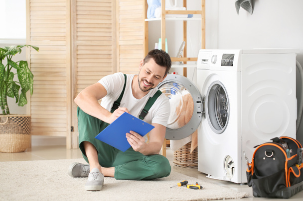 Worker repairing washing machine in laundry room - Фото, зображення