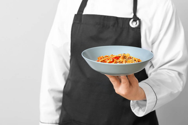 Handsome Asian chef with dish on grey background, closeup - Photo, image