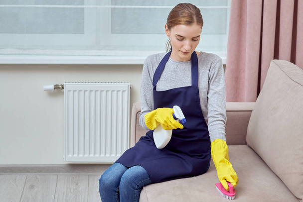 Girl sitting on the couch cleans the couch with a brush and household chemicals. - Foto, imagen