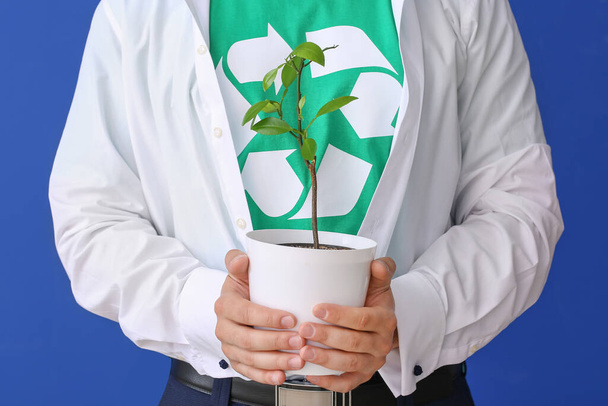 Man in t-shirt with recycling sign and plant on color background. Ecology concept - Foto, afbeelding