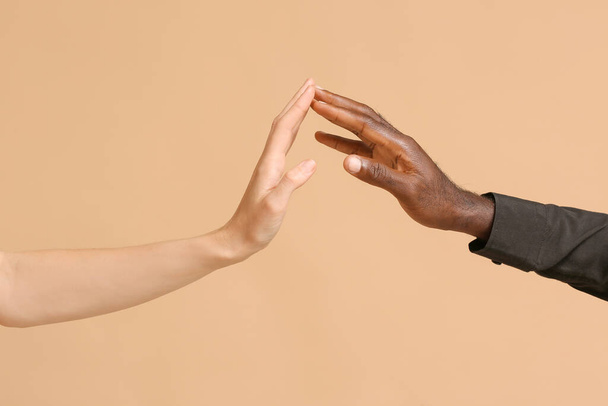 Mãos de mulher caucasiana e homem afro-americano estendendo a mão uns aos outros em fundo de cor. Conceito de racismo
 - Foto, Imagem