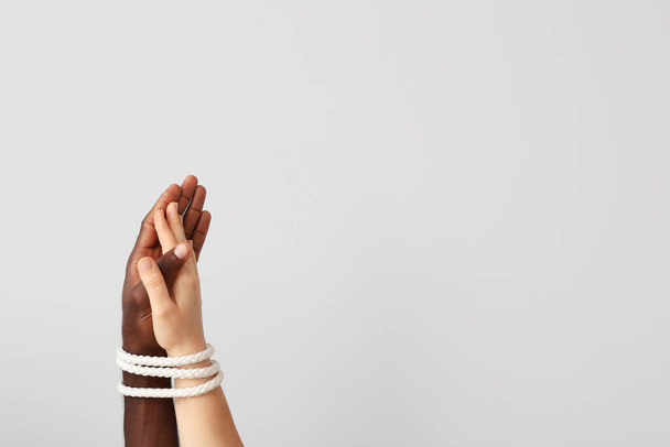 Valkoihoisen naisen ja afroamerikkalaisen miehen kädet sidottu yhteen köydellä kevyellä taustalla. Rasismin käsite - Valokuva, kuva